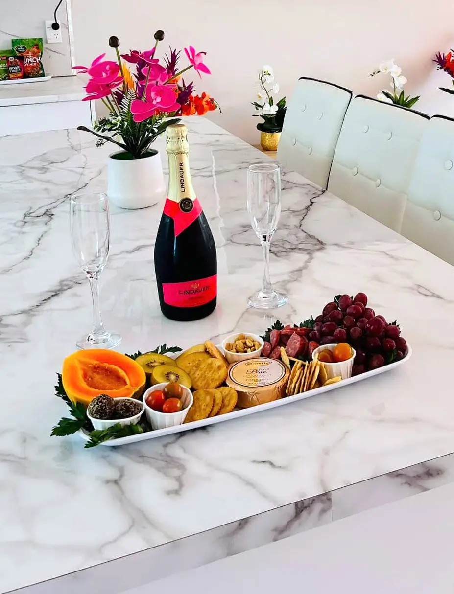 A platter of fresh fruit, cheese and crackers, alongside a bottle of champagne