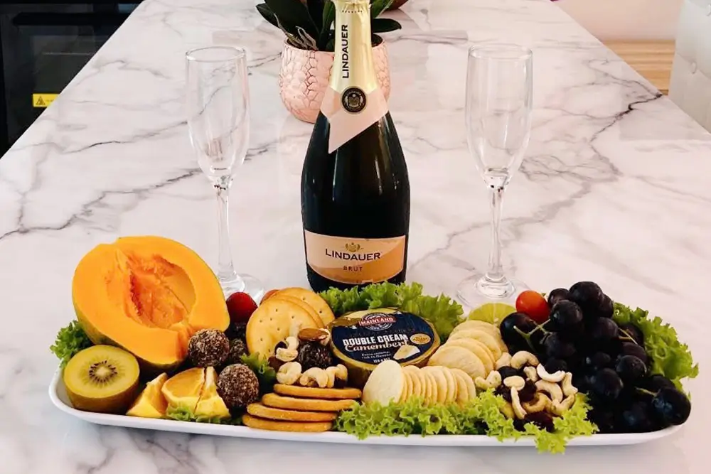A platter of fresh fruit, cheese and crackers, alongside a bottle of champagne